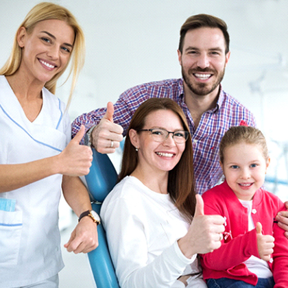 A mother, father, and little girl giving a thumbs up as they smile next to their pediatric dentist in West Brookfield