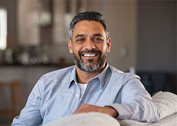 Man in blue shirt smiling on couch.