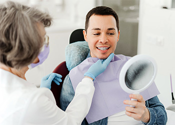 Man smiling at reflection in mirror with dentist.