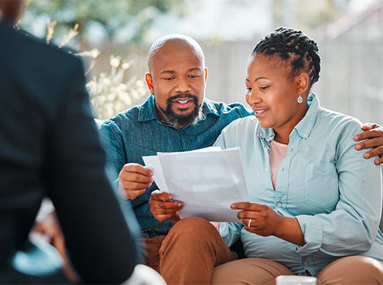 A man and woman sitting on a couch, reviewing dentistry-related papers together.